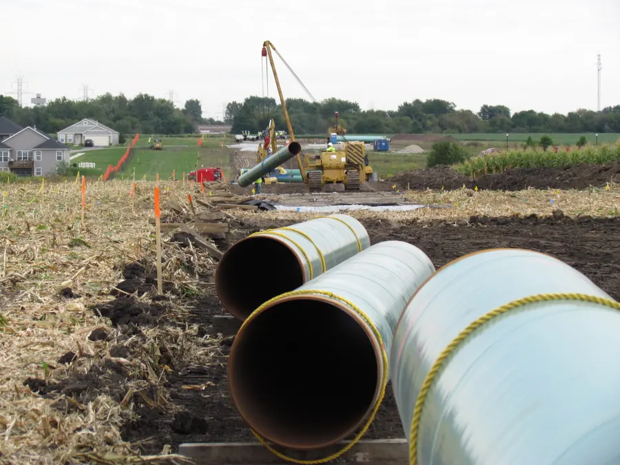 Coated pipeline sections staged along the right-of-way as a sideboom lowers pipe
